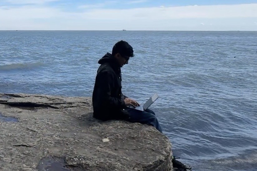 Russhil Chawla working on a laptop by the sea